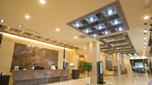 A modern hotel lobby with a marble reception desk, a large potted plant, and a high ceiling with recessed lighting. - Hotel International (Changwon)