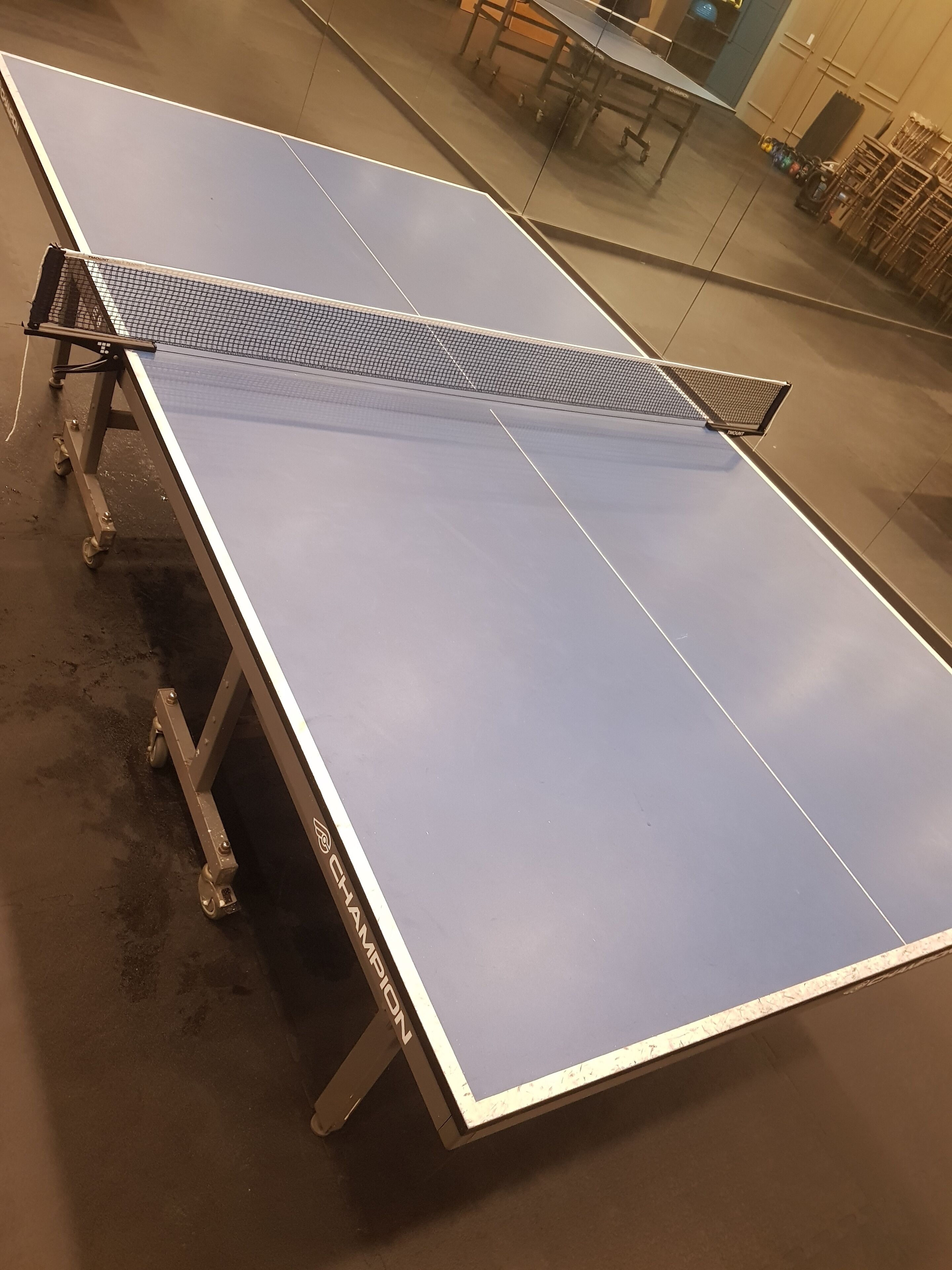 Una mesa de ping pong con ruedas, con la etiqueta 'Champion', en un espacio interior.