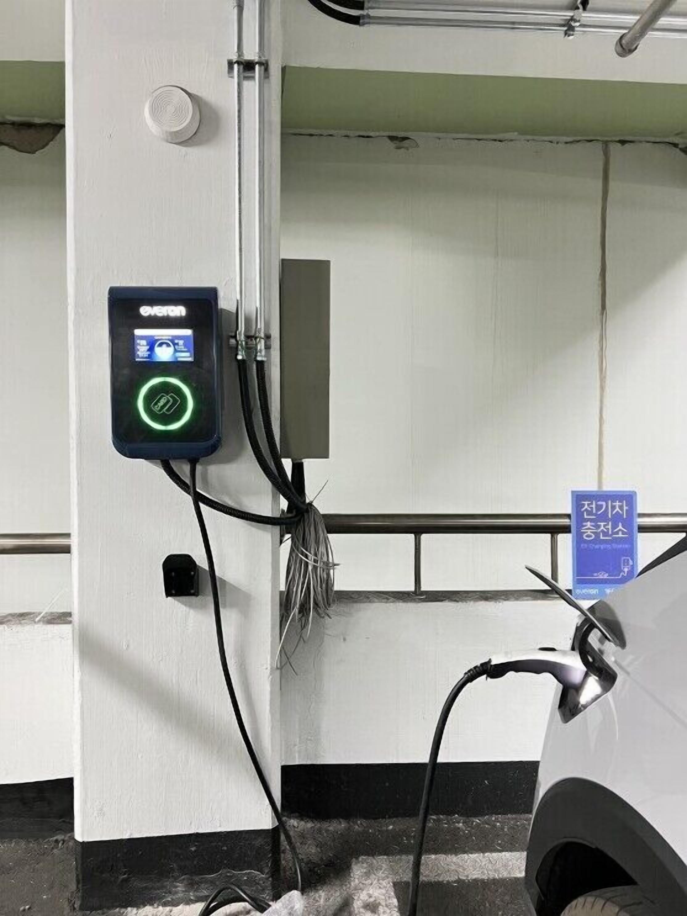 Een laadstation voor elektrische voertuigen met een digitaal scherm, een kabel en een bordje dat een parkeerplaats aangeeft.