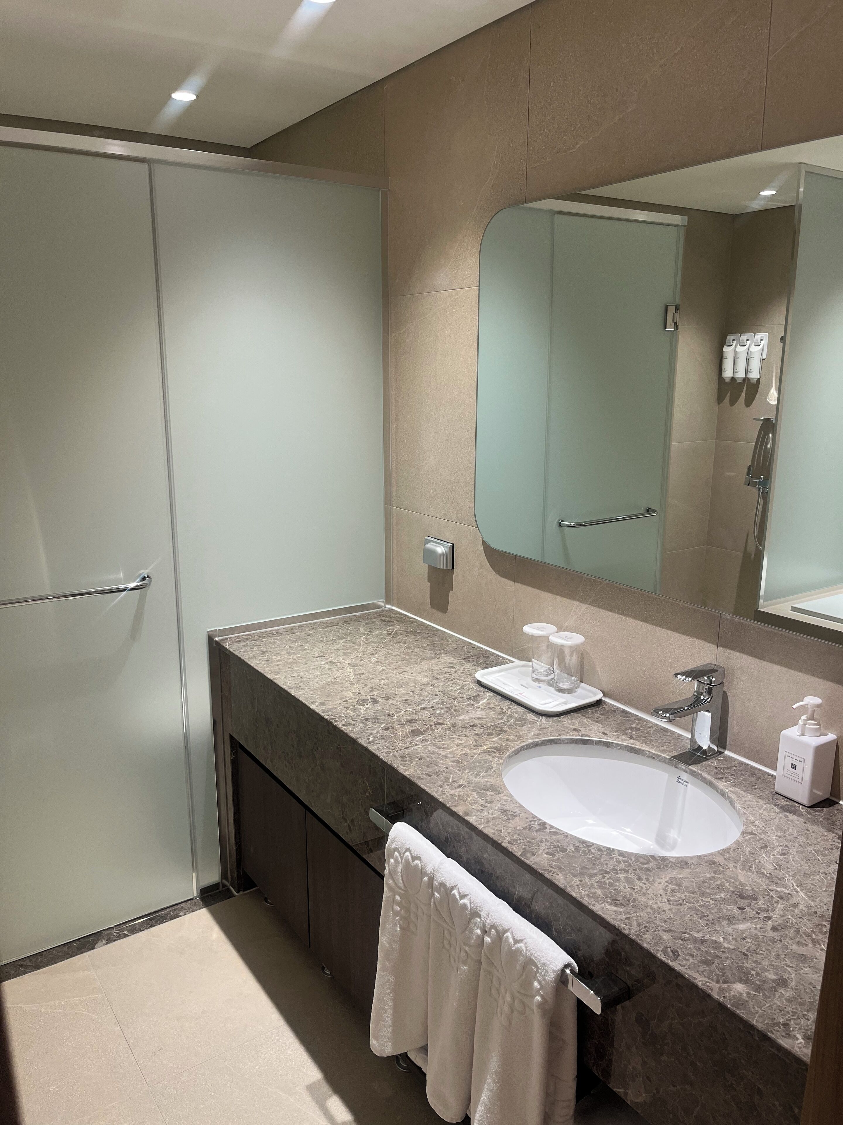 A modern bathroom with a marble countertop, a sink, a large mirror, and a shower area.