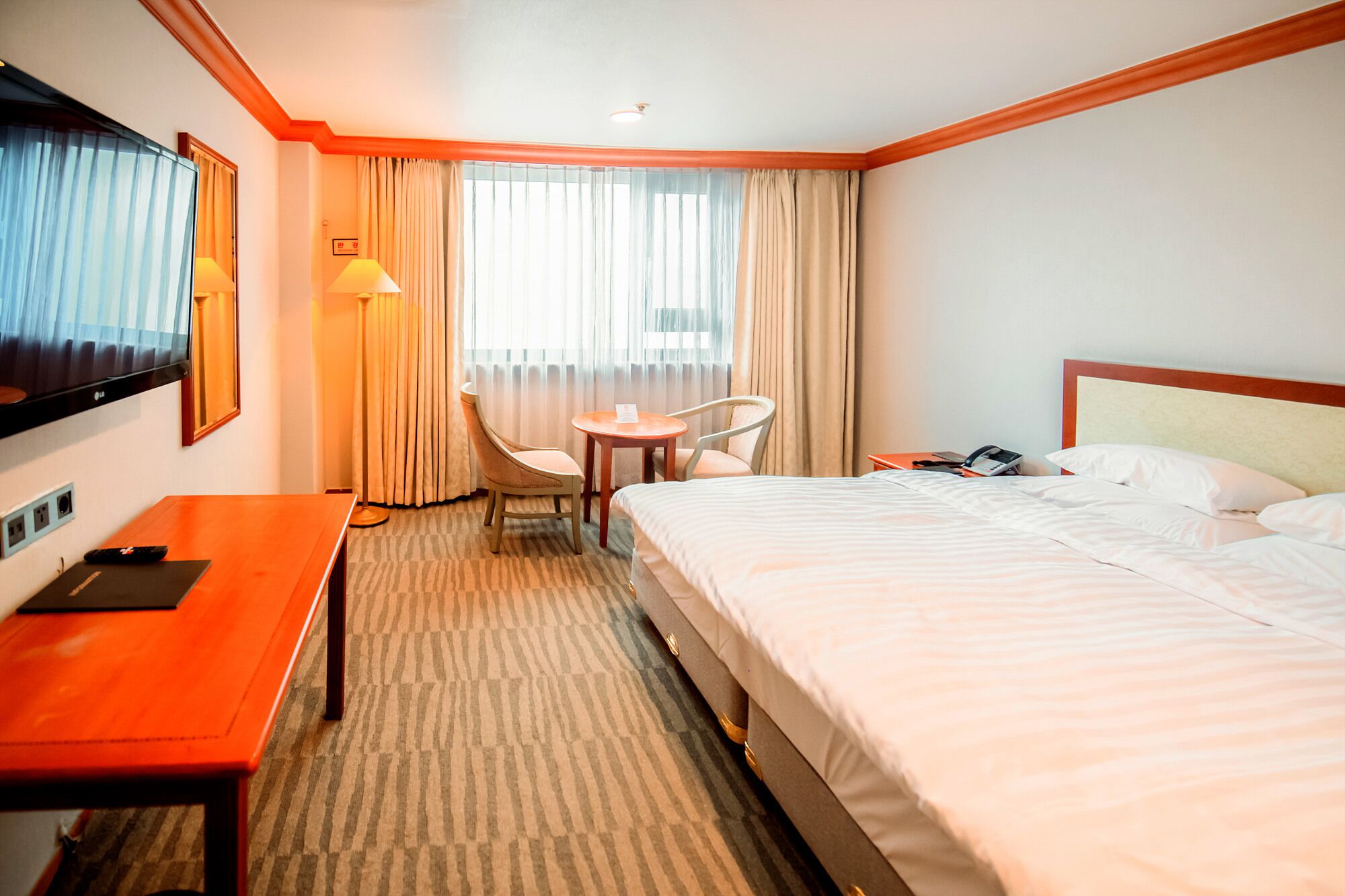 A hotel room with a bed, a desk, a chair, a TV, and a window with curtains.