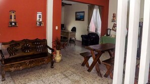 A living room with a wooden sofa, a dining table, and a coffee table. There is a painting on the wall and a window with curtains.