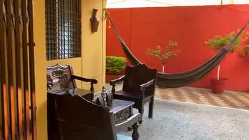 A yellow building with a red wall, a hammock, and two wooden chairs.