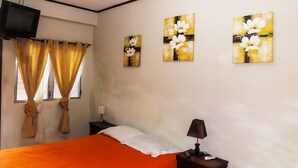 A bedroom with a bed, a TV, curtains, and artwork on the wall.