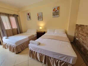 A hotel room with two beds, a nightstand, a lamp, and artwork on the wall. - La Posada B&B (San Pedro Sula)