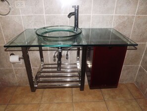 Un baño con lavamanos de vidrio, grifo cromado y un armario rojo.