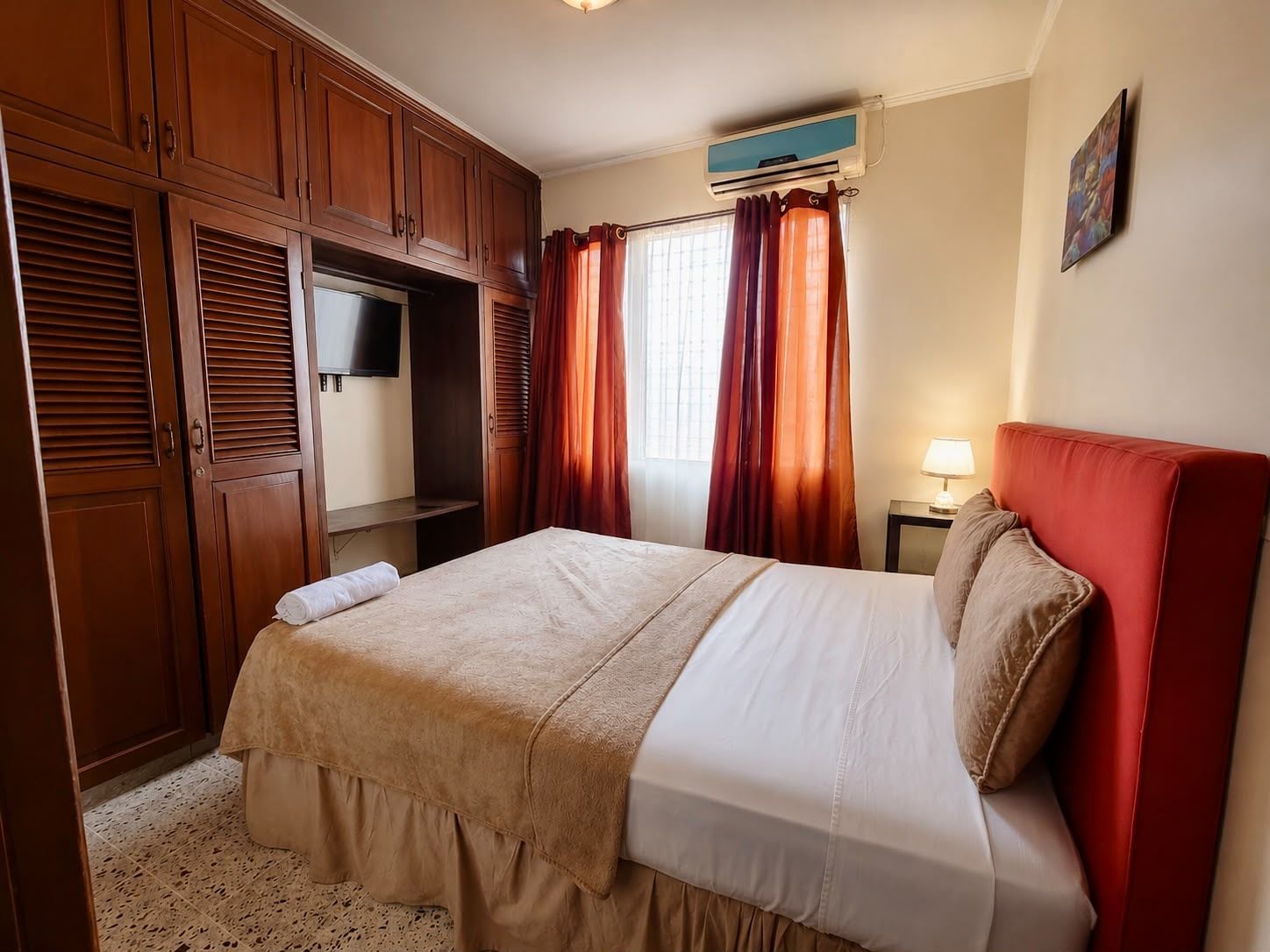 Ein Hotelzimmer mit Bett, Kleiderschrank, Fernseher und einem fenster mit Vorhängen.