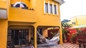 A two-story yellow building with a balcony, a hammock, and a pool.