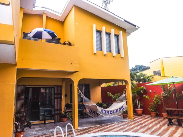 Un edificio amarillo de dos pisos con balcón, hamaca y piscina.