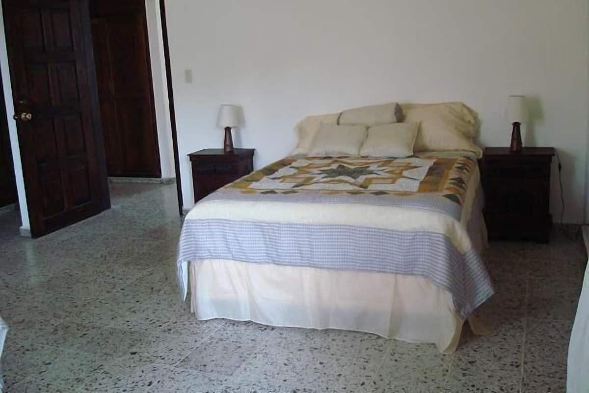 A bedroom with a bed, two bedside tables, a door, and a carpeted floor.
