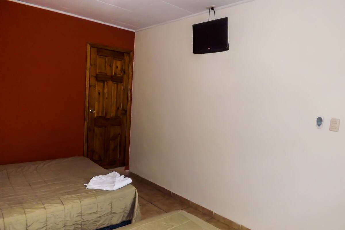 A room with two beds, a wooden door, a television, and a wall socket.
