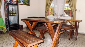 A wooden picnic table with benches in a room with a refrigerator and a painting on the wall.