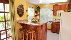 A kitchen with wooden cabinets, a marble countertop, and a central island with stools. - The Palms Oceanfront Suites (San Pedro)