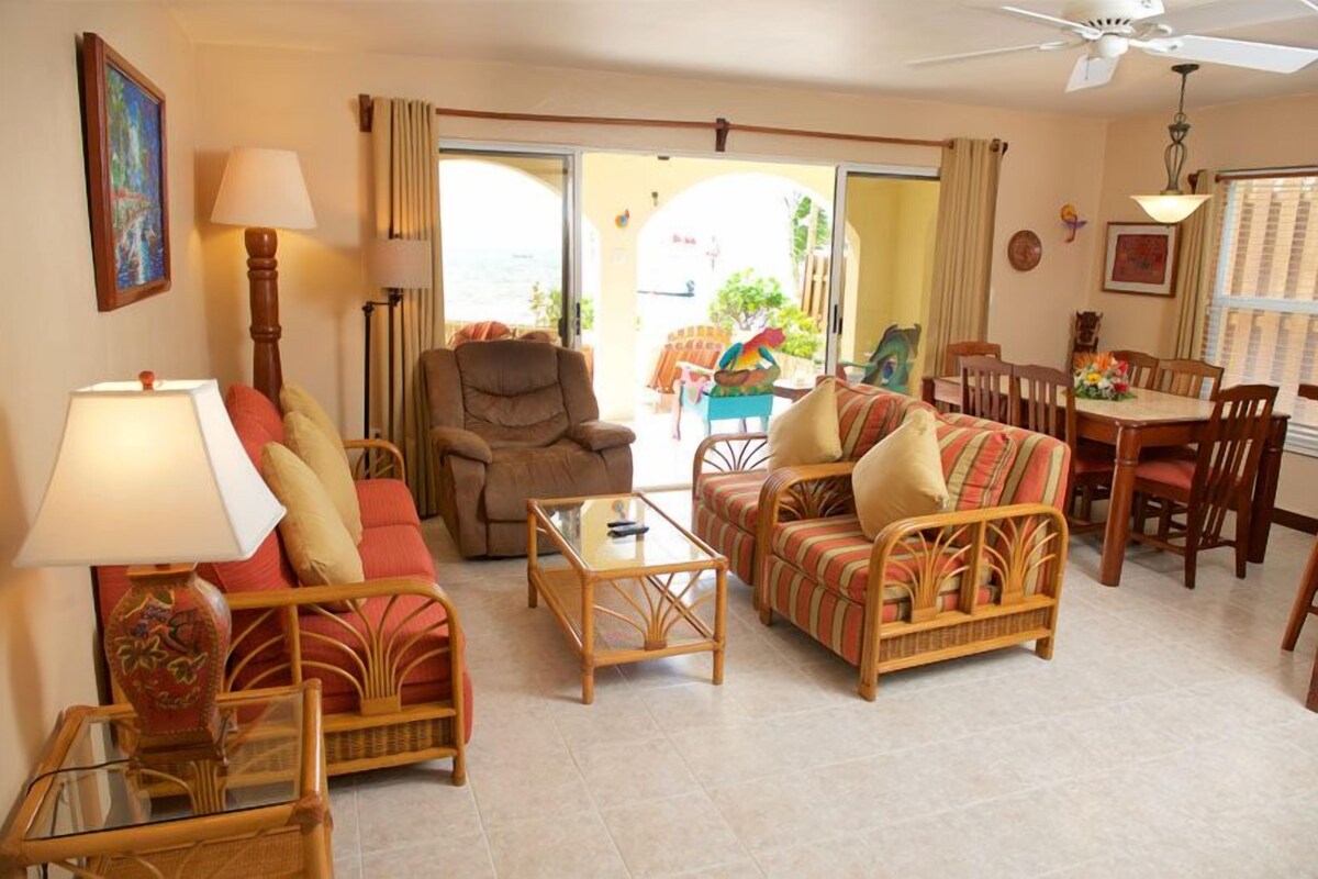 A living room with wicker furniture, a dining area with wooden chairs, and a ceiling fan.