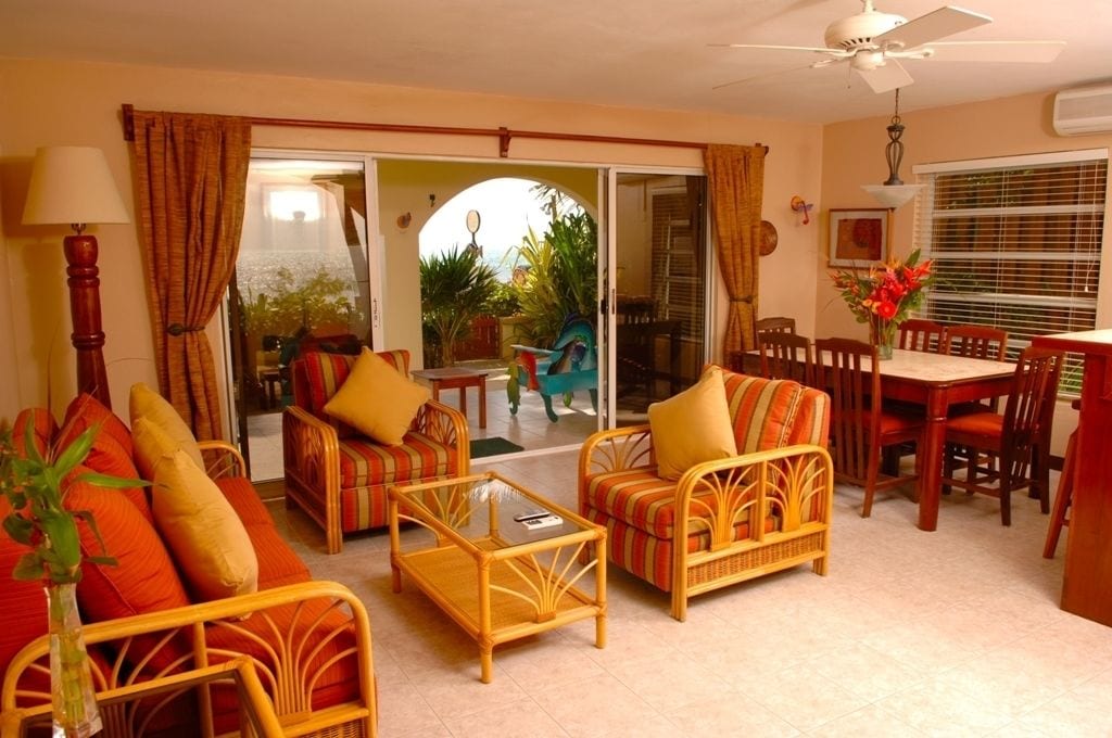 Sala de estar con muebles de mimbre, una mesa de comedor y sillas. Hay un ventanal corredero que da a un área exterior.