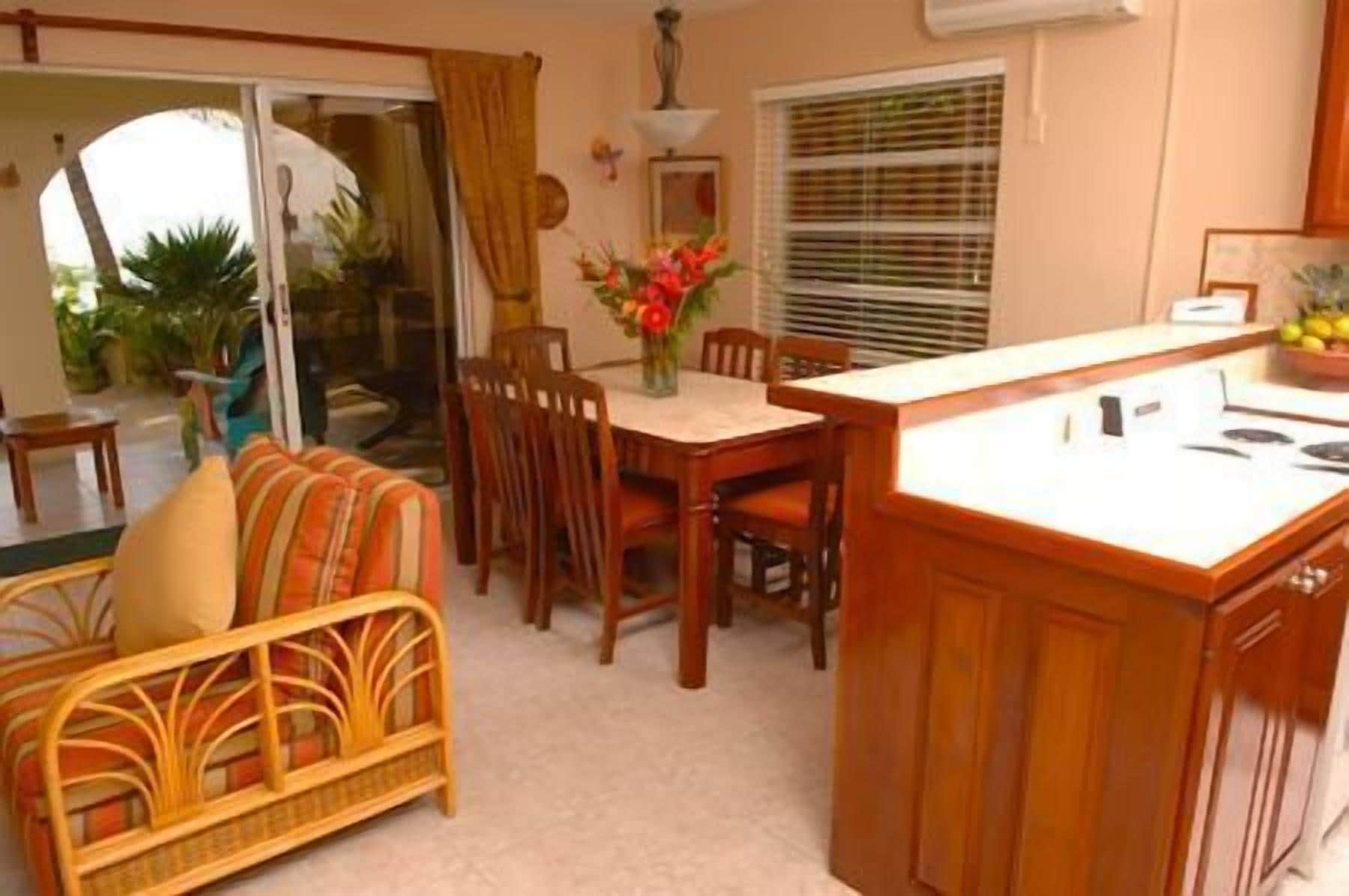 A cozy living room with a sofa, dining table, and chairs. There is a kitchen area with a stove and cabinets.