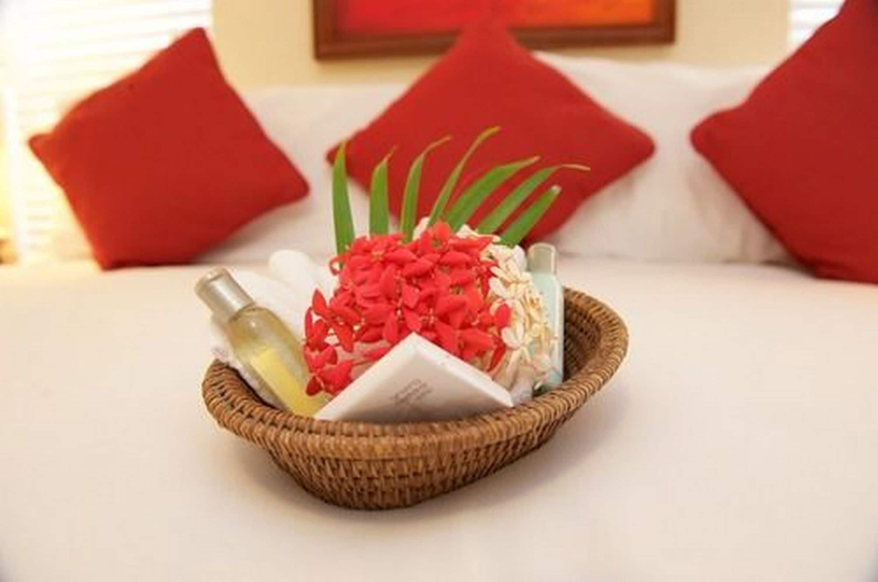 A basket with toiletries on a bed, surrounded by red pillows.
