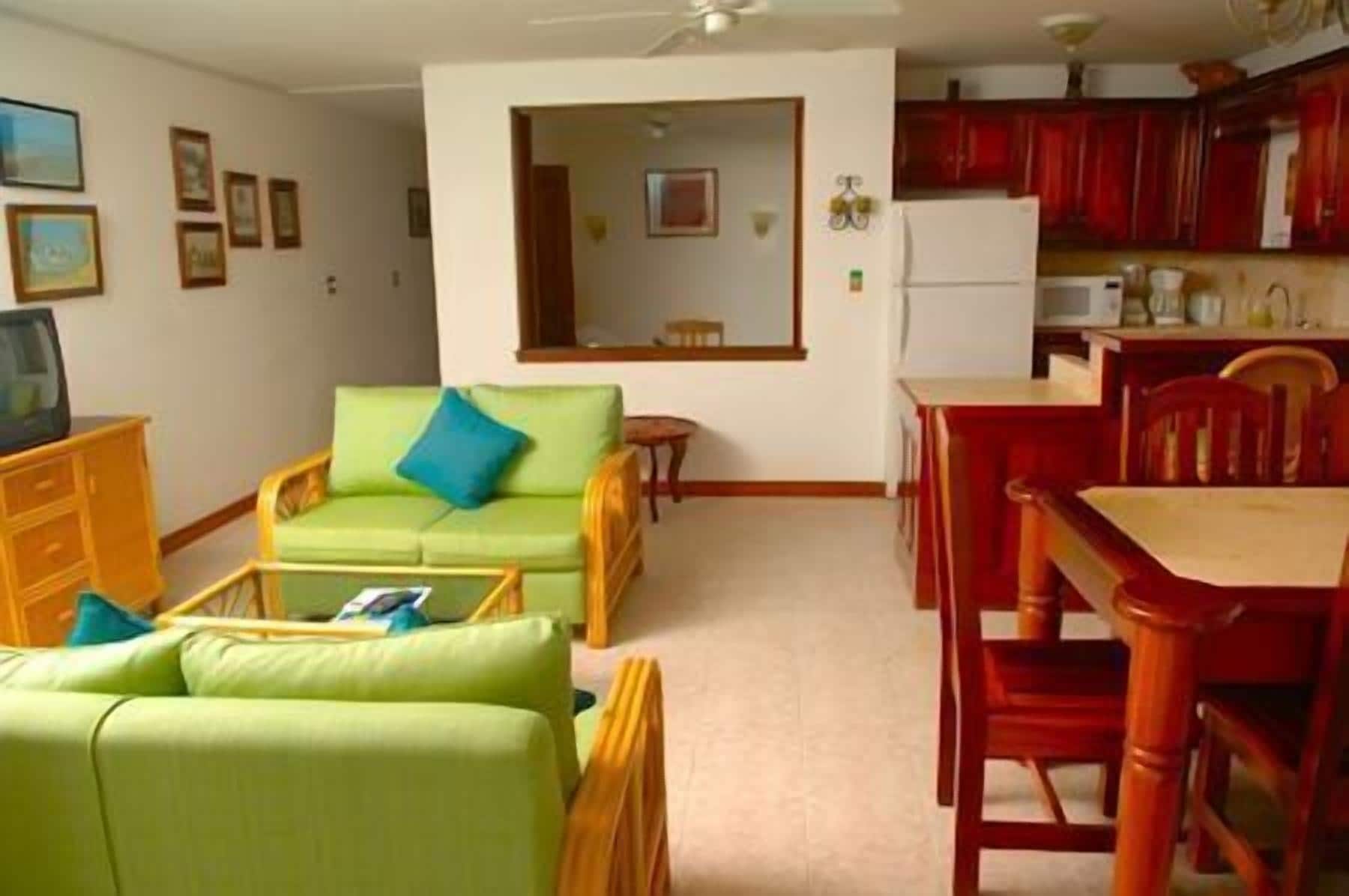 A living room with a green sofa, a dining table with red chairs, and a kitchen area with red cabinets.