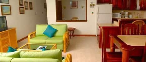 A living room with a green sofa, a dining table with red chairs, and a kitchen area with red cabinets.