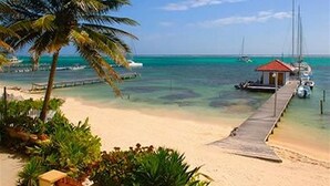 A beach with a wooden pier leading to a small red building, surrounded by palm trees and clear turquoise water. - The Palms Oceanfront Suites (San Pedro)