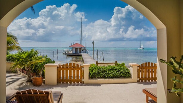 A view through an archway of a beachside area with a dock, a small building, and a sailboat in the distance. - The Palms Oceanfront Suites (San Pedro)
