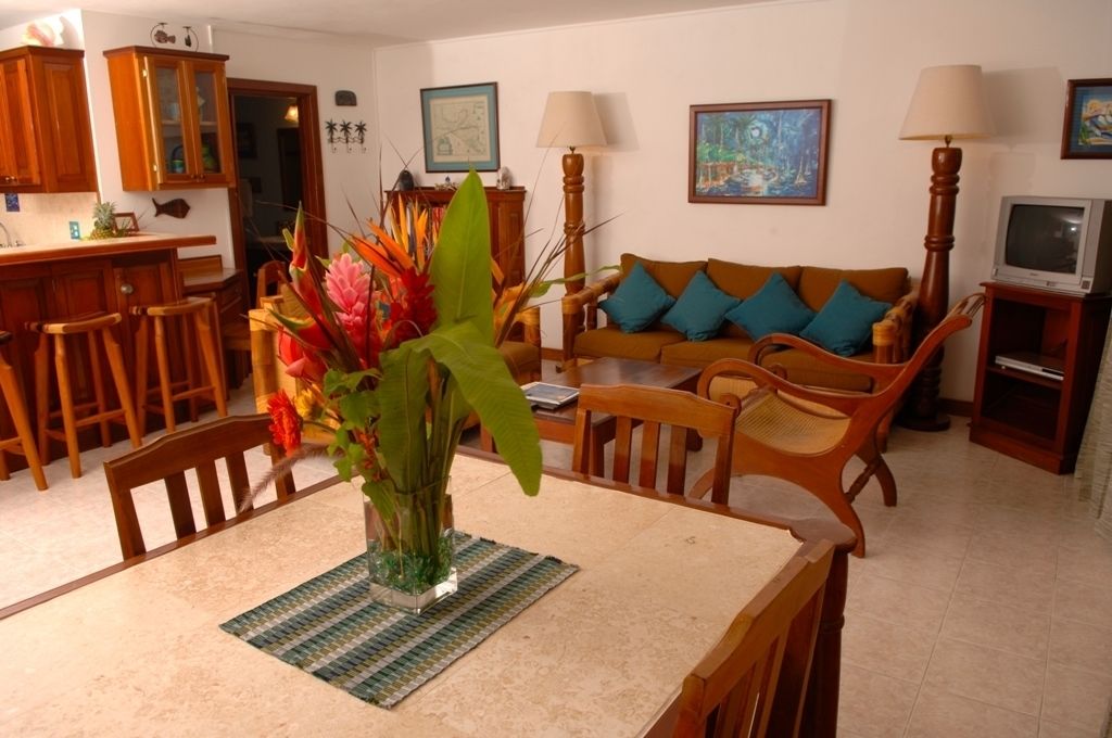 Un comedor con una mesa, sillas, un jarrón con flores, un aparador de madera y un sofá con cojines.