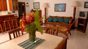 Un comedor con una mesa, sillas, un jarrón con flores, un aparador de madera y un sofá con cojines.