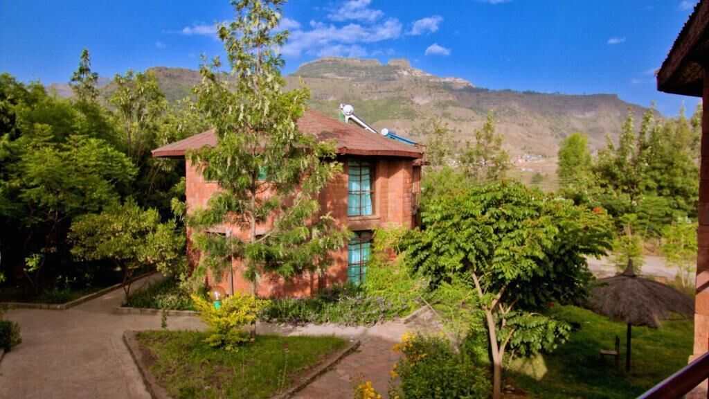 A two-story building with a red roof, surrounded by lush greenery and a mountainous backdrop.