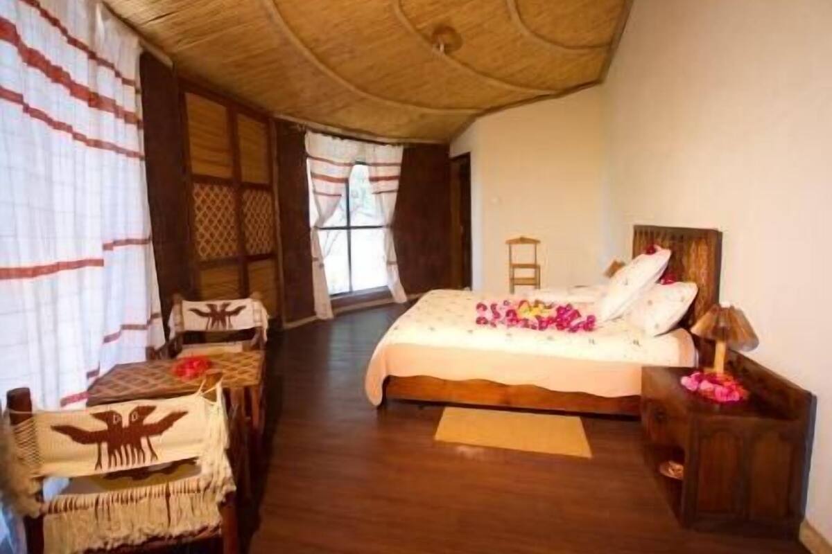 Een slaapkamer met een bed, een houten nachtkastje, een stoel en een raam met gordijnen.