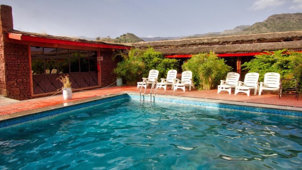 A swimming pool with lounge chairs, a stone building, and a thatched roof structure.