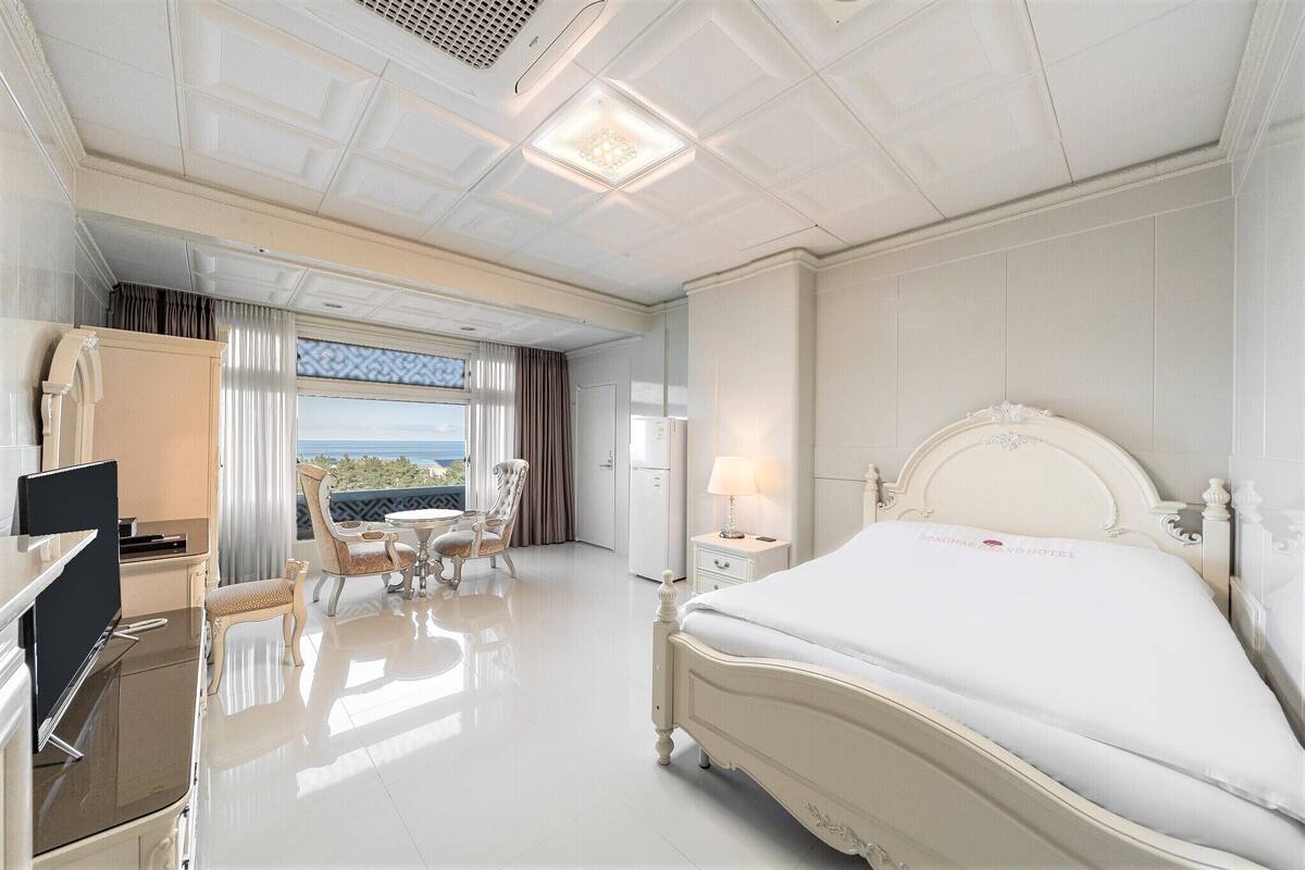 Ein Hotelzimmer mit einem großen Bett, einem Schreibtisch mit Fernseher, einem Sessel, einem kleinen Tisch und einem Fenster mit Blick.