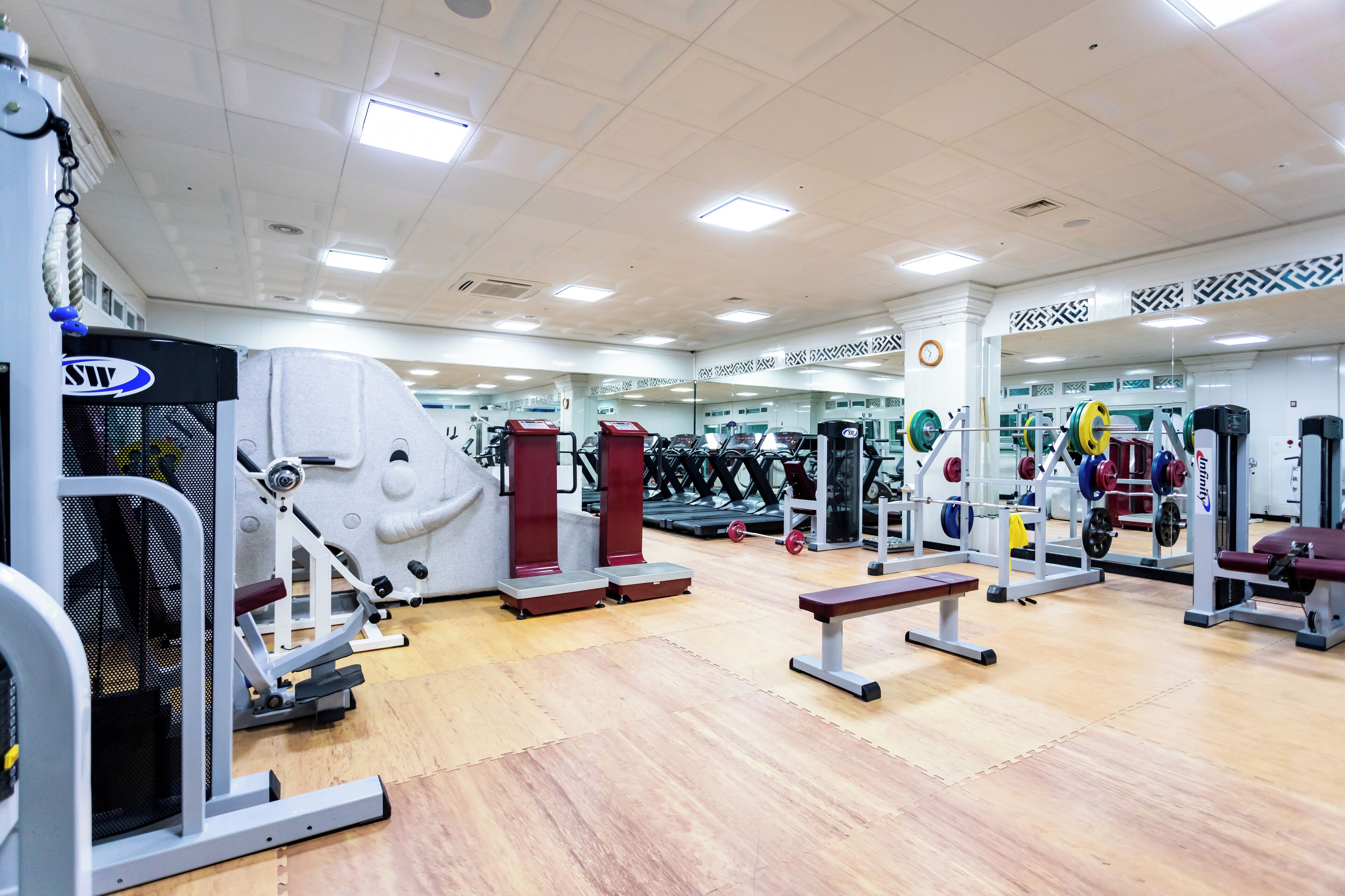 A gym with various exercise equipment, mirrors, and benches.