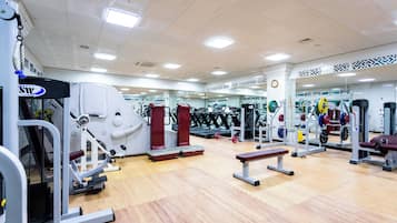 A gym with various exercise equipment, mirrors, and benches.