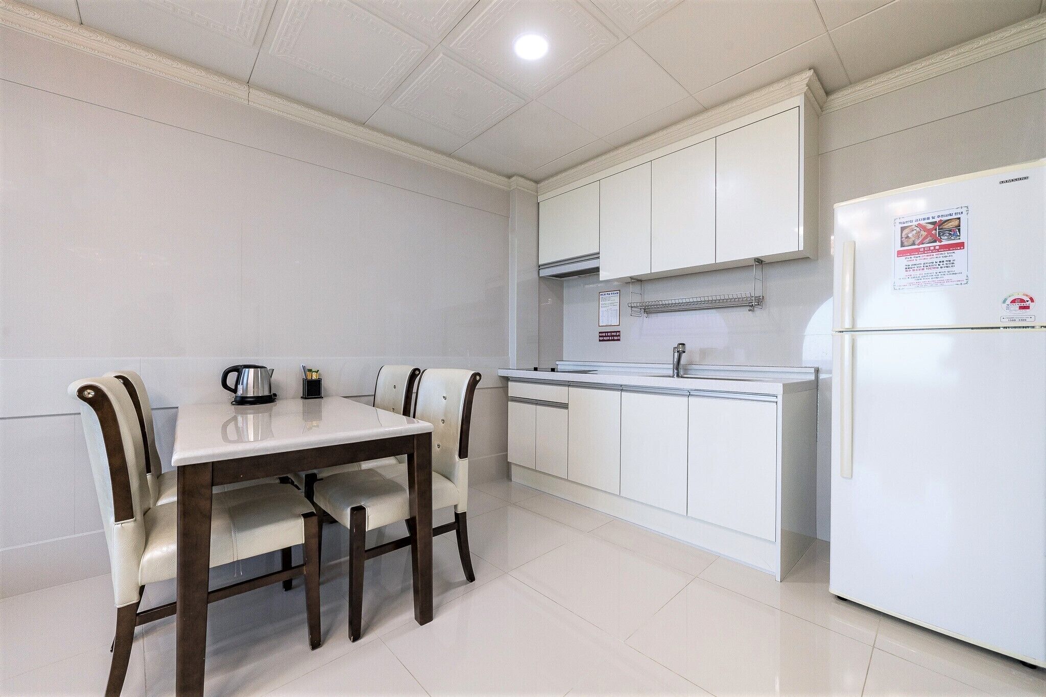 A modern kitchen with white cabinets, a white refrigerator, and a dining table with chairs.