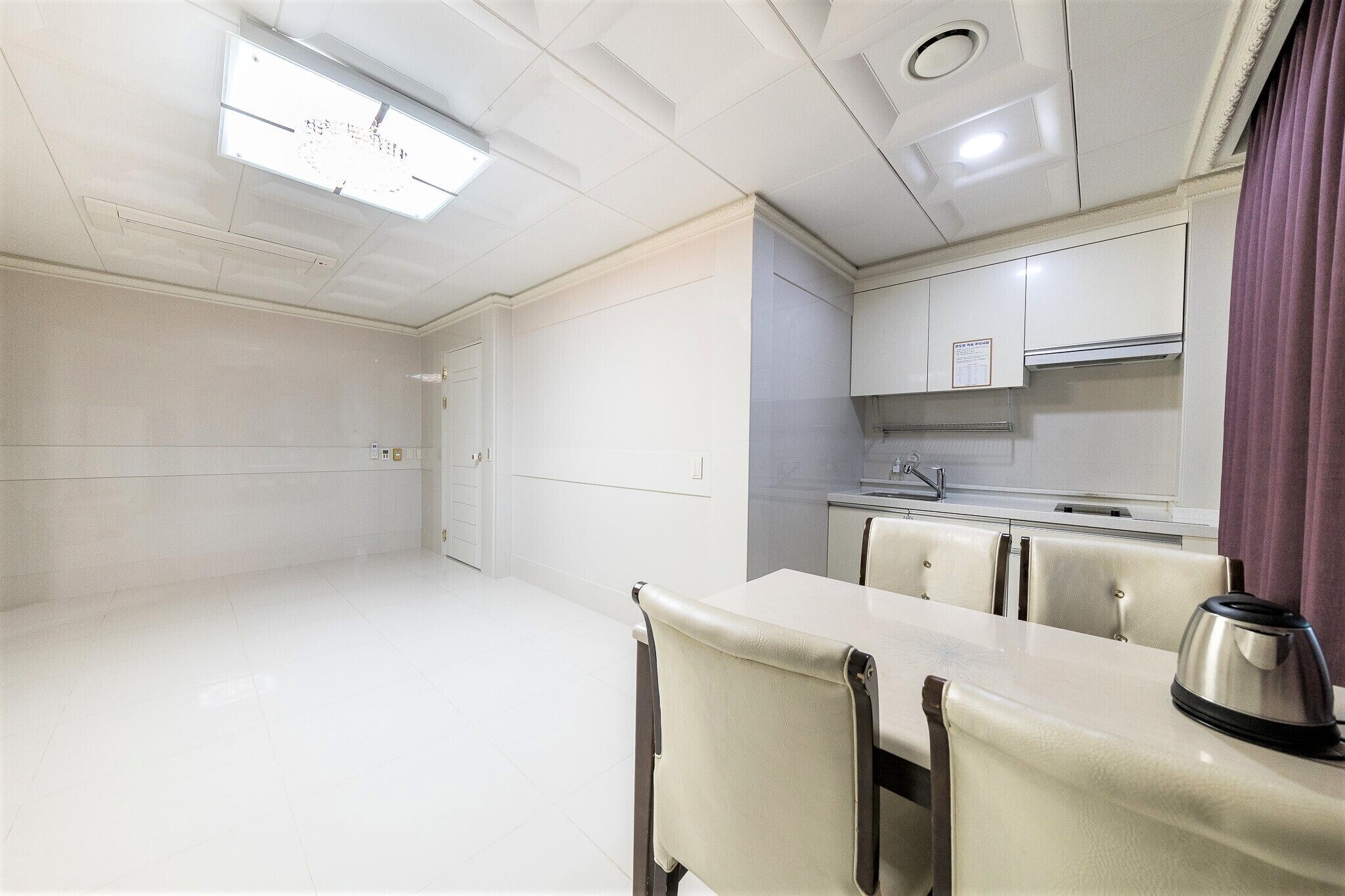 A compact kitchen with white cabinets, a small countertop, and a kettle.