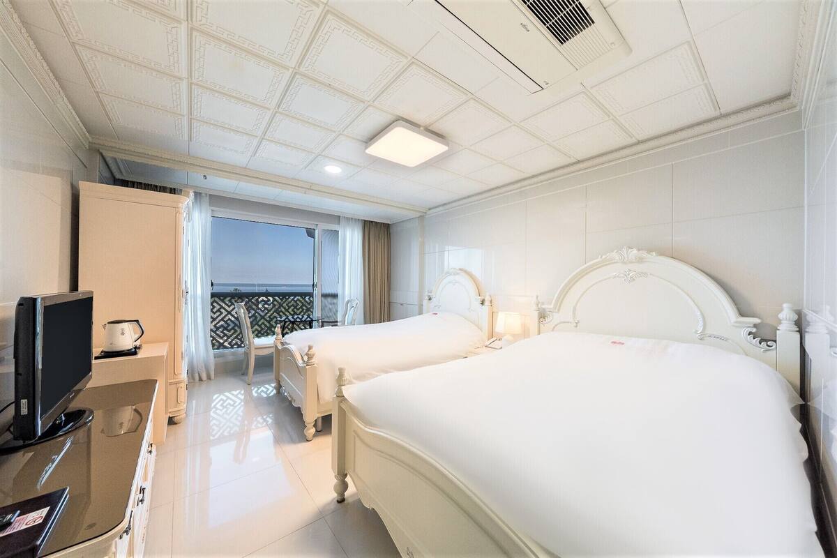 Ein Hotelzimmer mit zwei Betten, einem Fernseher, einem Schreibtisch und einem Balkon mit Blick.
