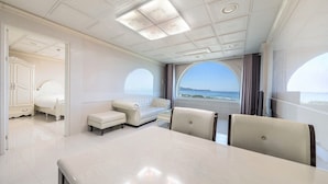 Ein luxuriöses Zimmer mit einem großen Bett, einer Sitzecke, einem Esstisch und Meerblick.