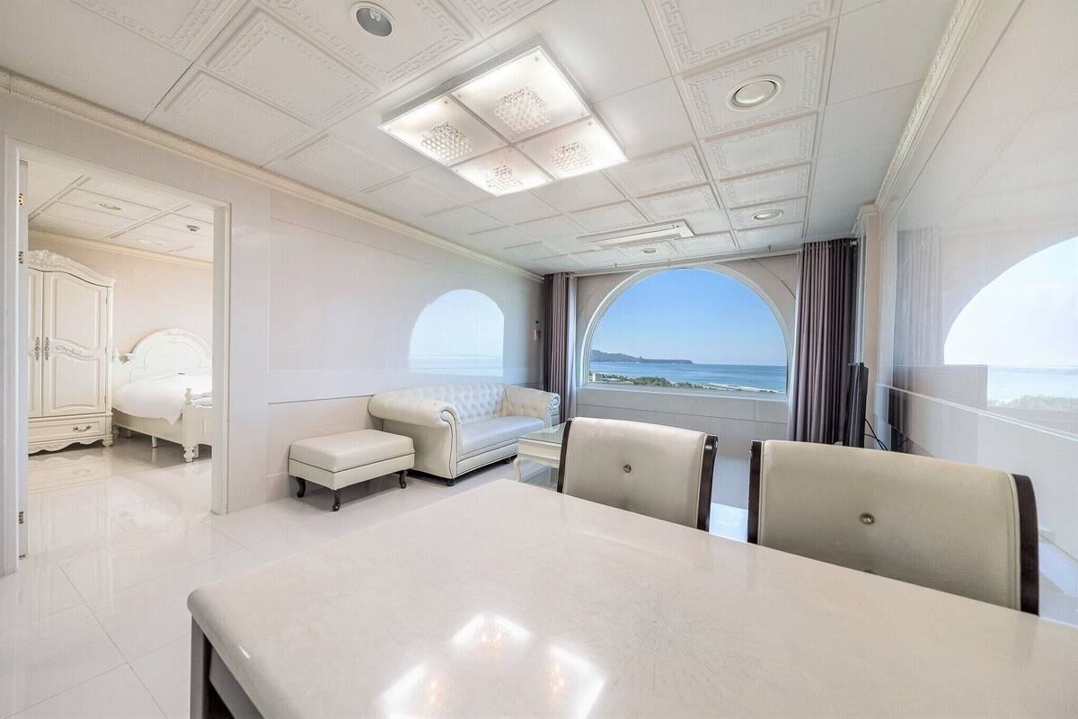 Ein luxuriöses Zimmer mit einem großen Bett, einer Sitzecke, einem Esstisch und Meerblick.