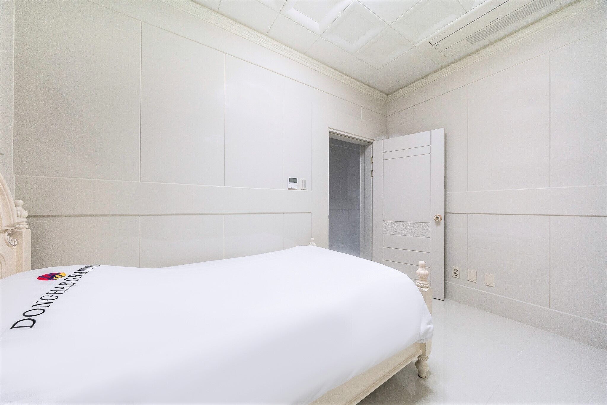 A bedroom with a bed, a nightstand, a door, and a light switch on the wall.
