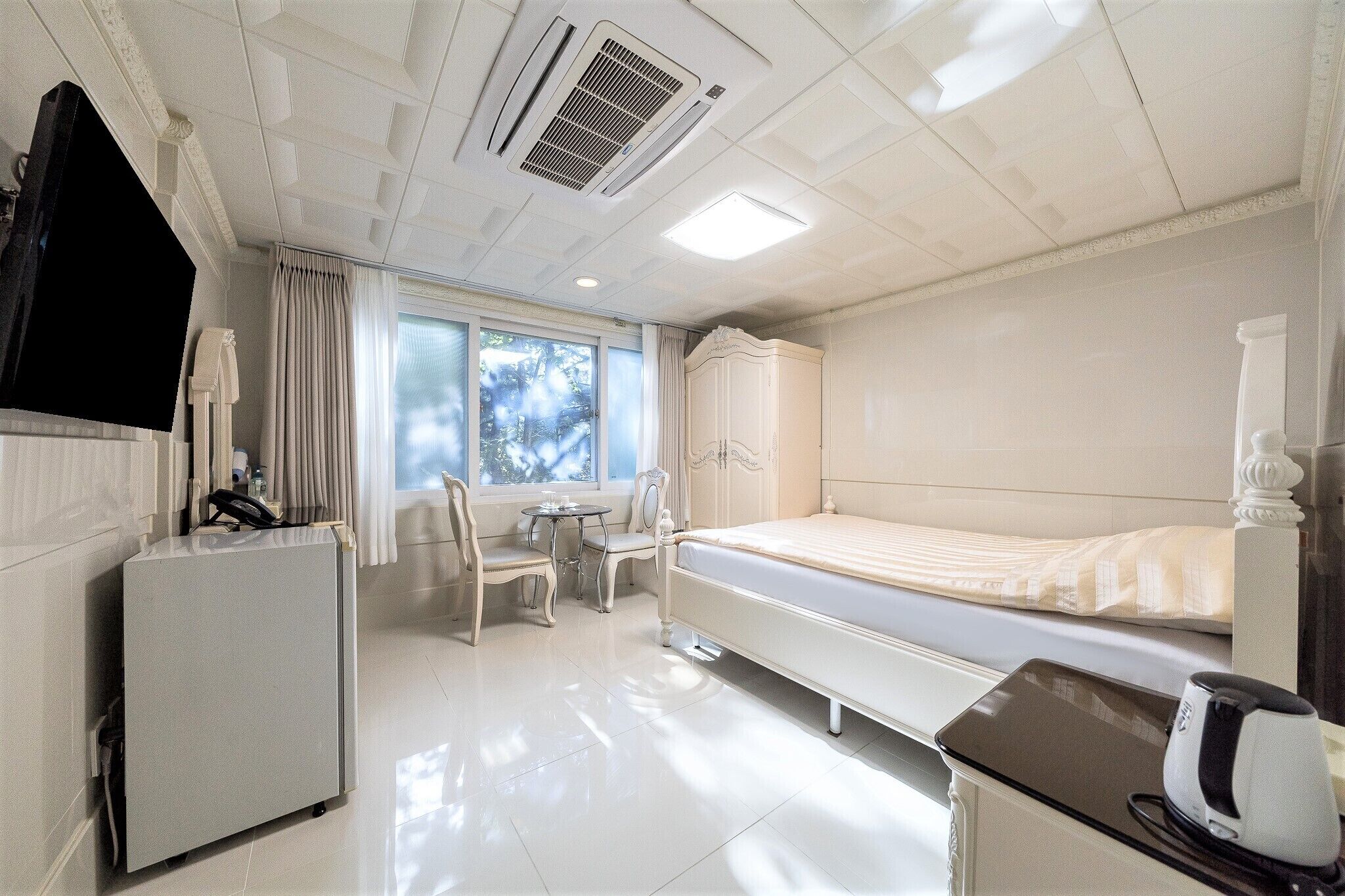 Una habitación de hotel con cama, escritorio, silla, armario y ventana con cortinas.