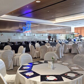 Une salle de banquet avec des tables rondes, des chaises et un espace cuisine à l’arrière-plan.
