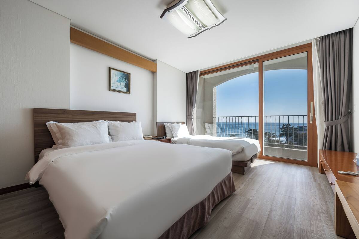Ein Hotelzimmer mit zwei Betten, einem Holzkopfende, einem großen Fenster mit Blick und einem Balkon.