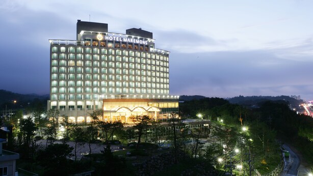 A multi-story hotel with a prominent sign at the top, a well-lit facade, and a landscaped area in front.