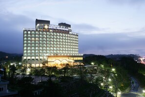Un hotel de varios pisos con un letrero llamativo en la parte superior, una fachada bien iluminada y un área ajardinada en la parte delantera.