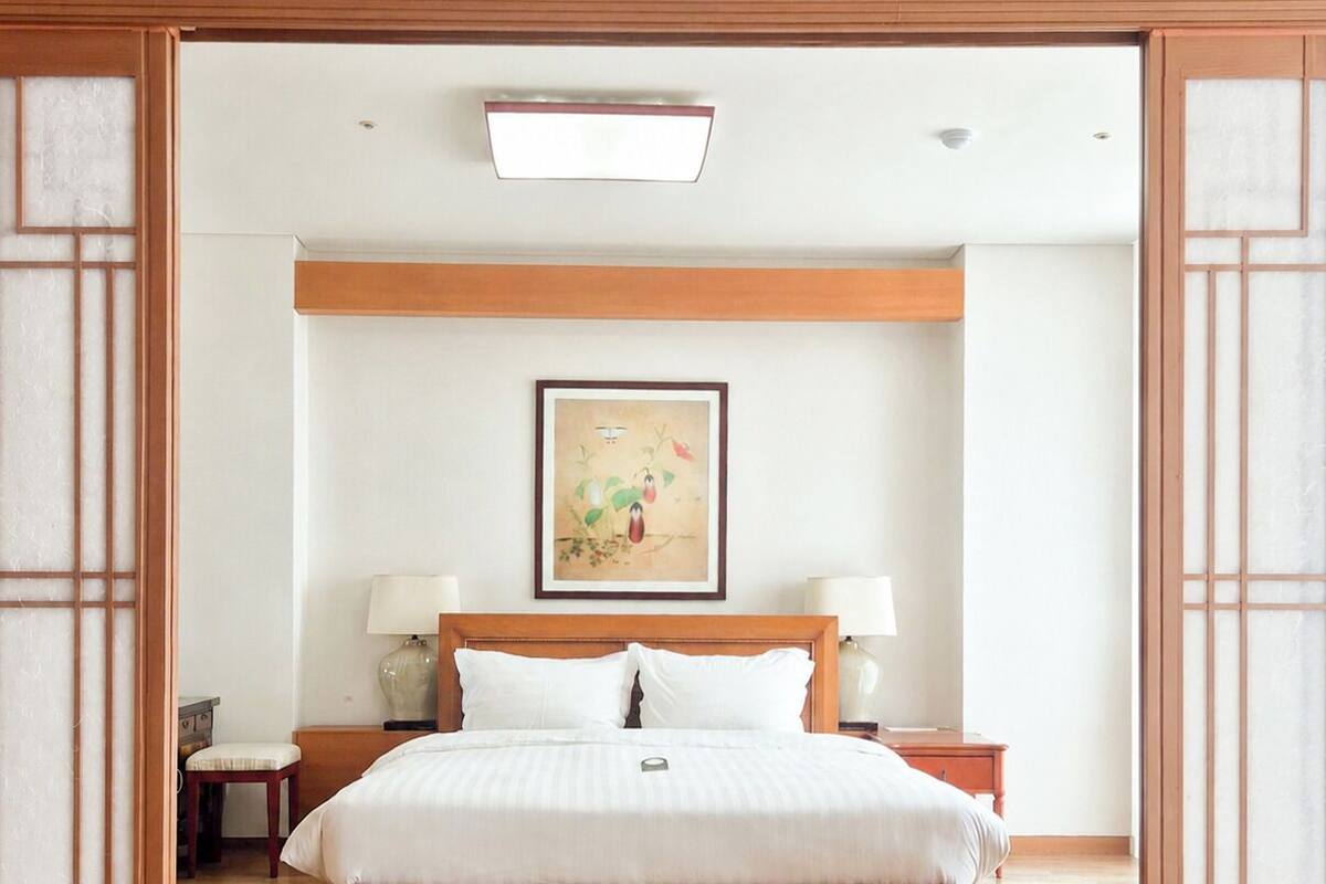 Ein Hotelzimmer mit einem Holzbett, Nachttischen, einem Beistelltisch, einem gerahmten Bild an der Wand und einer traditionellen Tür mit Glasscheiben.