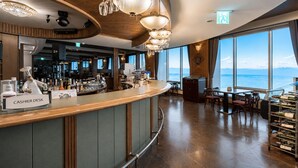 A bar area with a cashier desk, large windows, and a view of the sea.