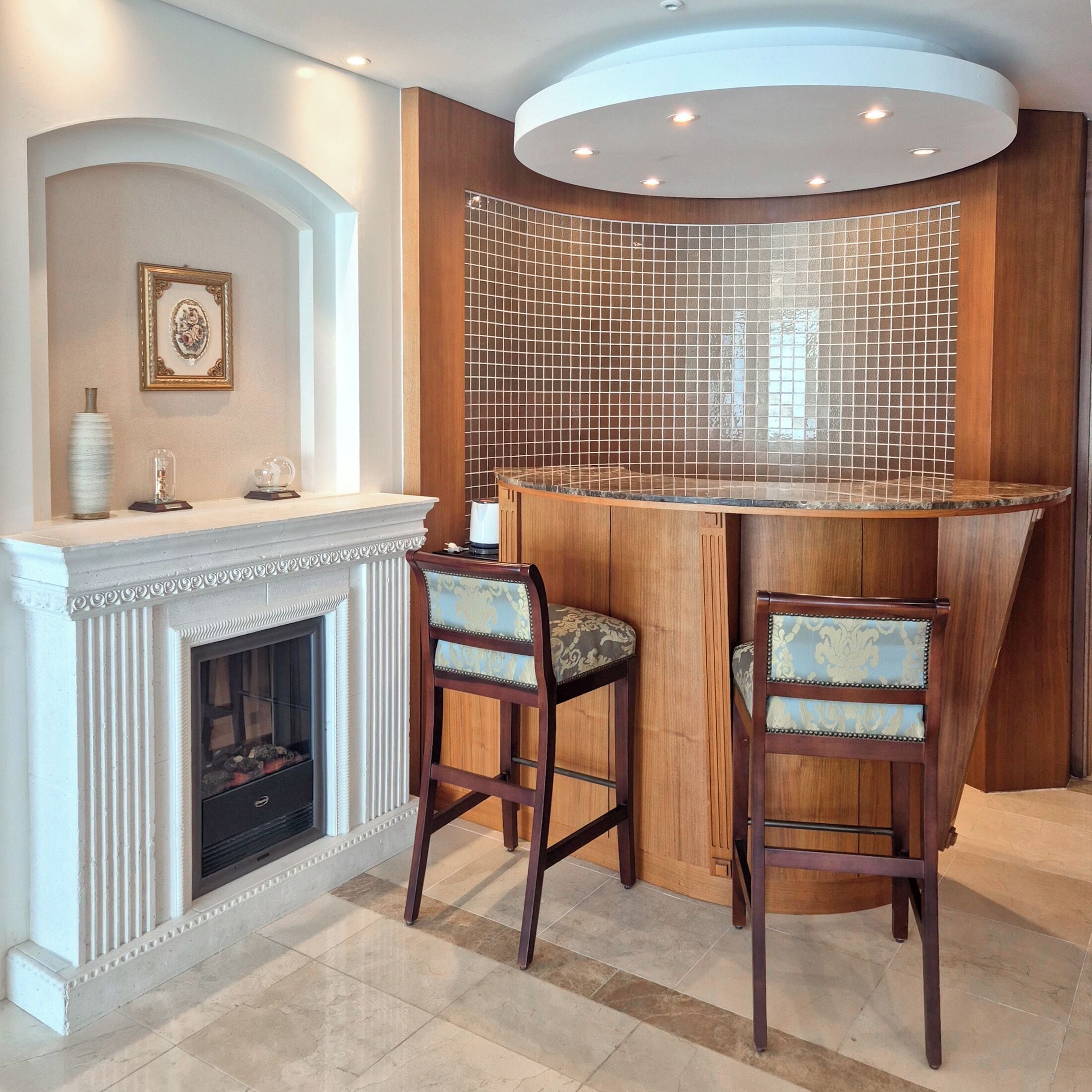 Una zona de bar con chimenea, dos taburetes altos y una pared decorada con azulejos.