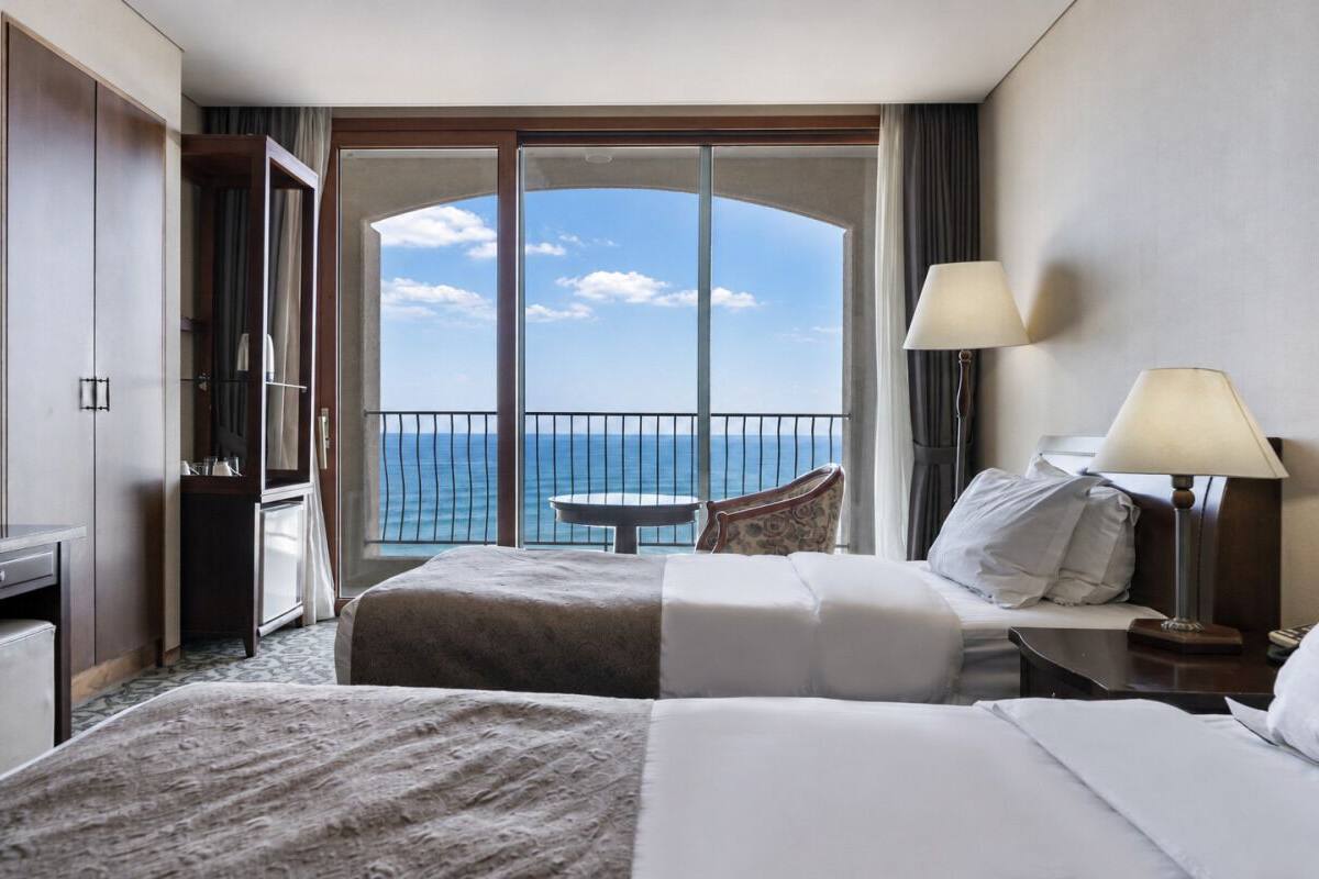 Ein Hotelzimmer mit Balkon, zwei Betten, einem Schreibtisch und einem Stuhl.