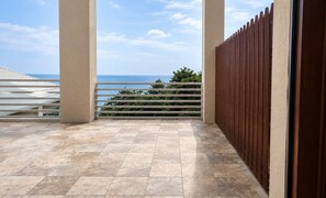 Un balcon avec vue sur la mer, une clôture en bois et un sol carrelé.