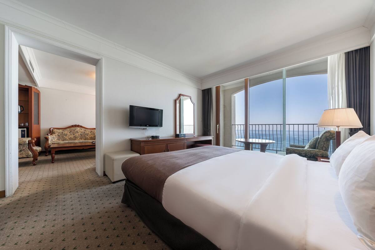 Ein Hotelzimmer mit einem großen Bett, einem Fernseher, einem Schreibtisch, einem Stuhl und einem Balkon mit Blick.